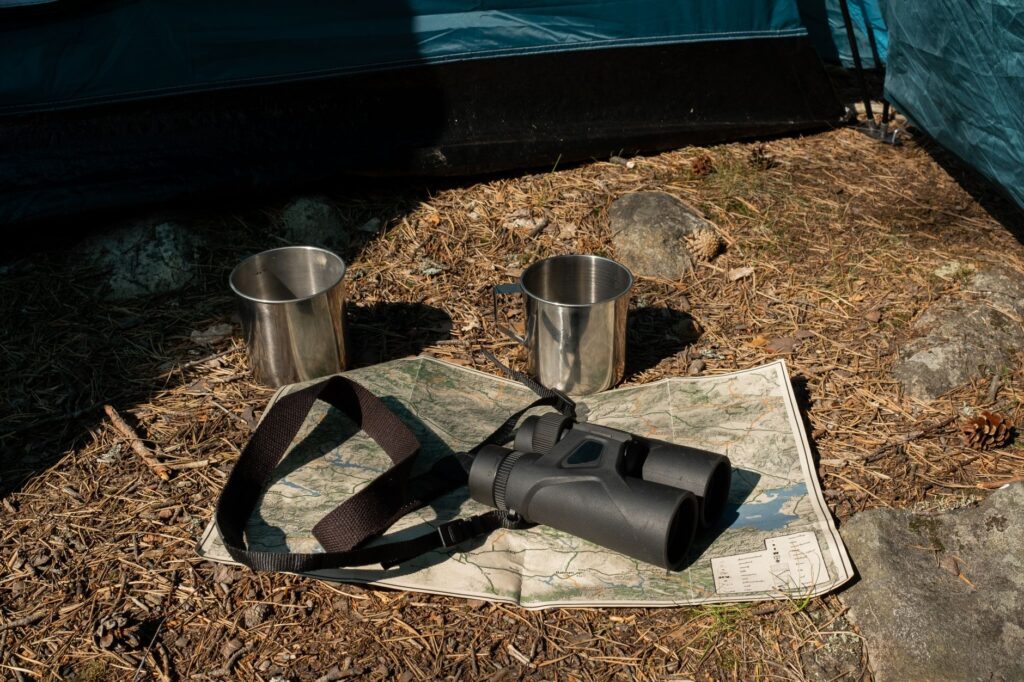 Close-up of camping gear, including binoculars, map, and cups outside a tent.