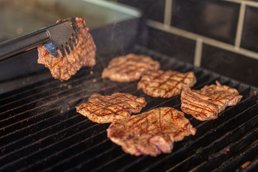 Close-up of juicy beef steaks being grilled, showcasing smoke and grill marks.