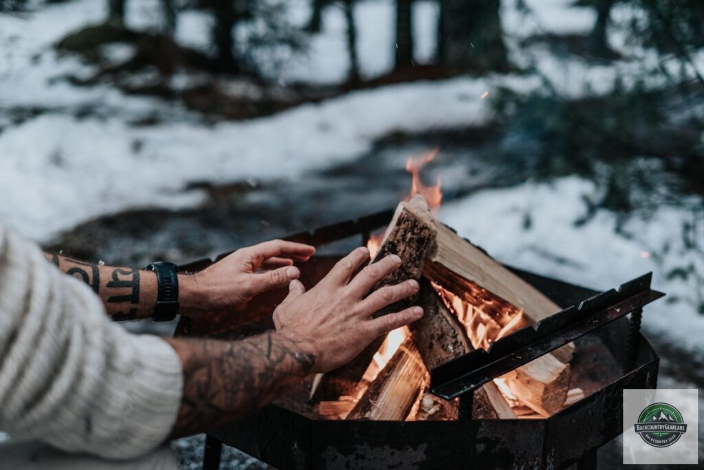 Tattooed hands warming by a campfire in a snowy Lithuanian forest.