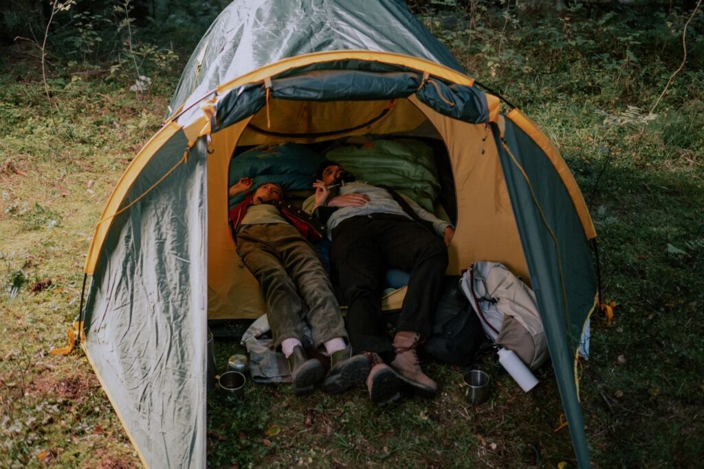 A man and woman lying together in a tent amidst a lush green forest, enjoying a peaceful camping experience.