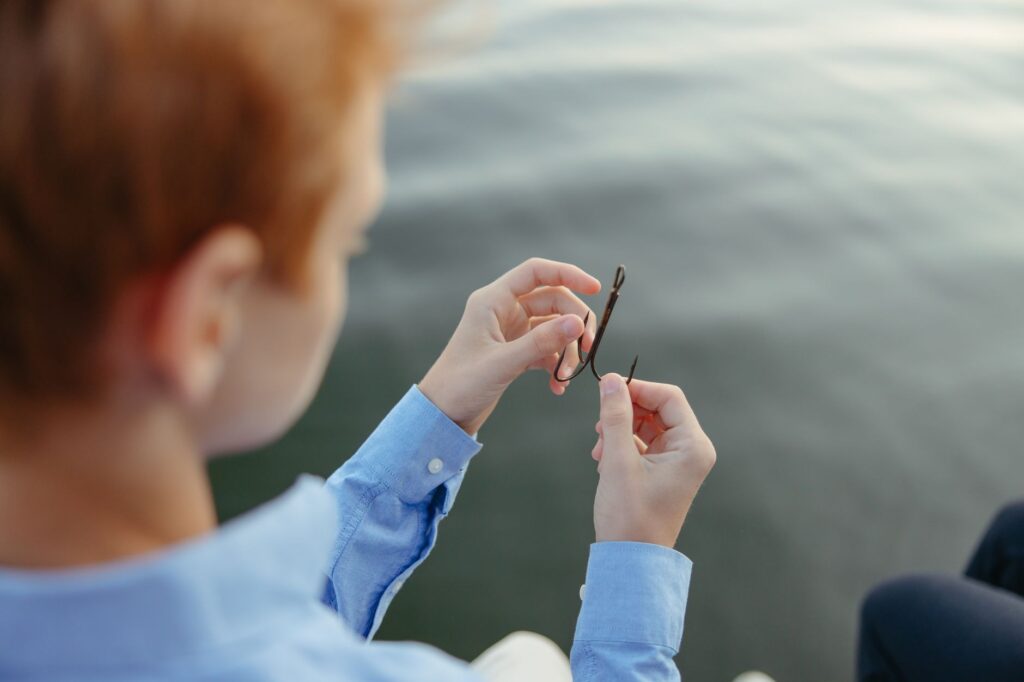 Close-up of a person handling fishing hooks near the water. Perfect for outdoor lifestyle images.