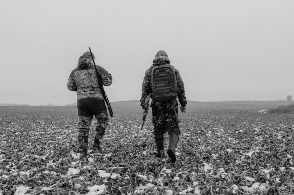 Two hunters in camouflage walking through a snowy field in winter.