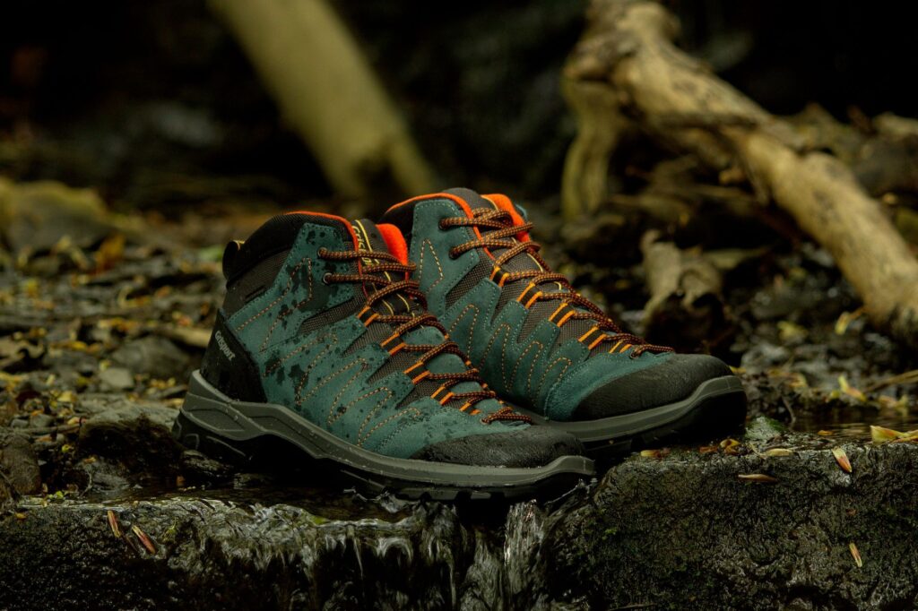 Teal hiking boots with orange laces in natural riverbed setting in England.